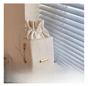 Détail du sac seau crème montrant les coutures ondulées et la bandoulière chaîne
