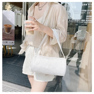 Detailed close-up of white cylindrical shoulder bag with floral embossed jacquard texture