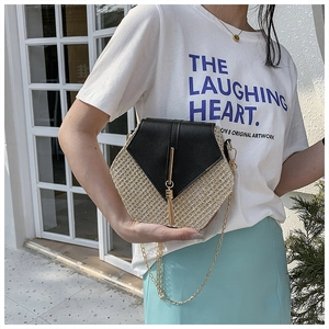 Detail of a hexagonal woven straw crossbody bag with black leather flap and metal tassels
