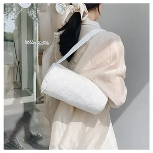 Detailed view of white floral jacquard cylindrical shoulder bag on a female model