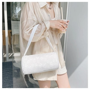 Detail of white cylindrical shoulder bag featuring intricate lace floral texture and top zipper