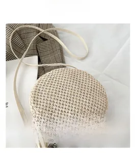 Dettaglio della borsa a tracolla rotonda in paglia beige con zip in metallo e nappa