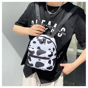 Close-up of a mini cow print canvas backpack worn by a model in a casual street style