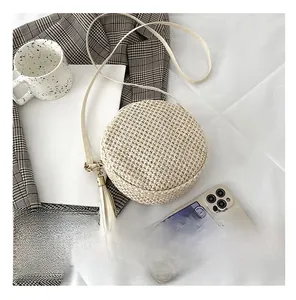 Dettaglio della piccola borsa a tracolla in paglia beige con nappe vicino allo smartphone