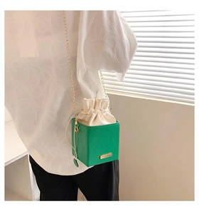 Détail d'un sac seau vert gaufré avec fermeture à cordon et bandoulière chaîne dorée