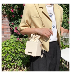Détail d'un sac seau crème avec chaîne dorée porté sur un blazer jaune élégant