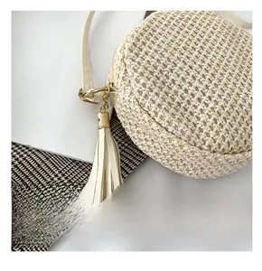Dettaglio della borsa rotonda in paglia beige con zip e ciondolo a nappina
