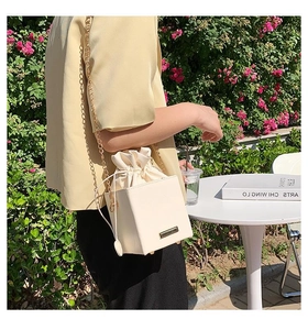 Détail d'un sac seau blanc crème avec fermeture à cordon et bandoulière chaîne dorée
