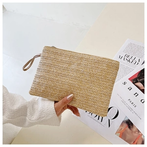 Handheld view of woven straw clutch with herringbone texture and wrist strap