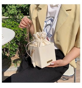 Détail d'un sac seau blanc crème avec texture ondulée et bandoulière chaîne dorée