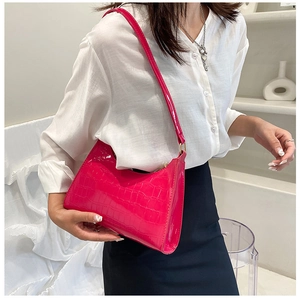 Detail of fuchsia crocodile pattern shoulder bag with glossy finish on a white background