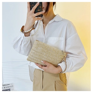 Macro detail of hand-woven wheat straw clutch bag with leather wrist strap and zip closure