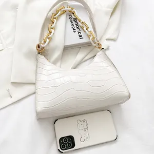 White crocodile pattern shoulder bag with chunky acrylic chain next to a smartphone