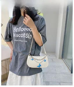 Sac baguette crème avec chaînes papillon en argent porté par un mannequin au soleil