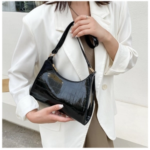 Detail of black glossy crocodile pattern faux leather shoulder bag on white blazer