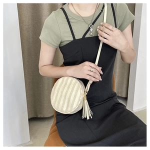 Dettaglio di una borsa a tracolla rotonda intrecciata con trama a righe e grande nappa