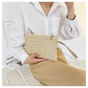 Detail of handmade woven straw clutch bag with leather wrist strap and metal zipper