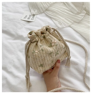 Détail d'un sac seau tissé beige avec broderie florale et fermeture par cordon de serrage