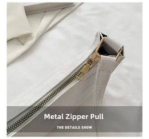 Close-up of golden metal zipper pull on white crocodile embossed small square bag