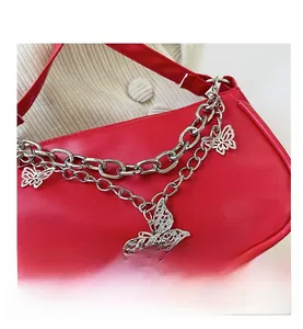 Détail du sac rouge sous le bras avec doubles chaînes argentées et pendentifs papillons