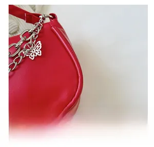 Détail du sac à main en cuir rouge avec grosse chaîne argentée et pendentif papillon