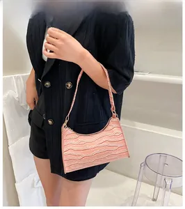 Pink crocodile-embossed baguette bag styled with a black suit on a female model