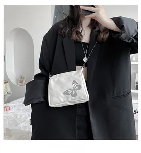 Detailed close-up of white crossbody bag with reflective butterfly print and zipper