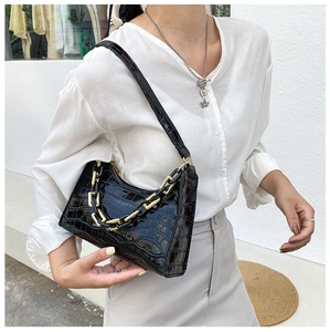 Detail of black crocodile texture handbag featuring thick gold and black decorative chain