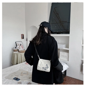 Detail view of a white canvas crossbody bag with grey butterfly print and silver chain strap