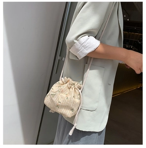 Détail du sac seau en paille tressée avec broderie florale et bandoulière à cordon blanc