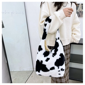 Detail of soft plush cow print tote bag shown held by a model in a minimal interior