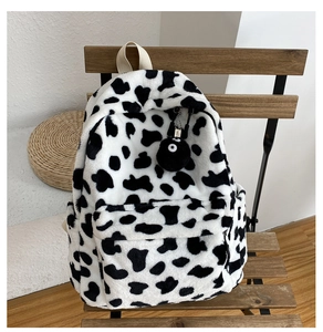 Dettaglio di uno zaino in peluche con motivo mucca bianco e nero e un grazioso ciondolo pompon