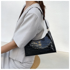 Detail view of the black crocodile pattern patent leather shoulder bag on a model