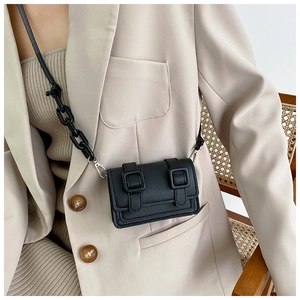Detail of a black mini square bag with resin chain and leather straps on a model