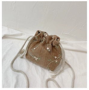 Detail der gewebten Stroh-Eimertasche mit Blumenstickerei und weißem Kordelzug-Gurt