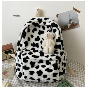 Dettaglio dello zaino in peluche a macchie di mucca con ciondolo a orso e spalline