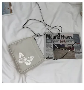 Detail of light grey square crossbody bag with silver reflective butterfly and rope strap