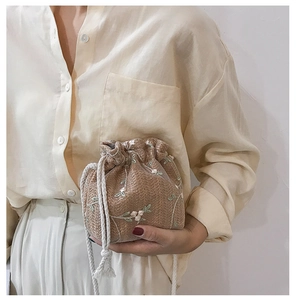 Détail du sac seau en paille tissée main avec broderie florale en dentelle et cordon de serrage