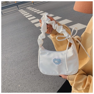 Detail of white hobo bag with pleated handle, ribbon bow, and cartoon whale patch