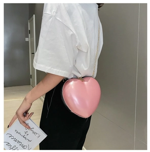 Detail of pink heart-shaped bag with glossy finish and golden chain strap on a model