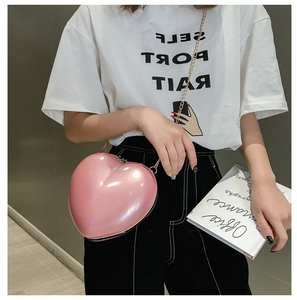 Detailed shot of a pink heart-shaped mini clutch with gold chain strap worn by a model