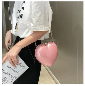 Detail of pink heart-shaped chain bag with glossy finish and gold metal strap