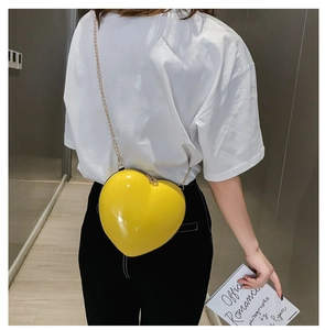 Detail of yellow heart-shaped crossbody bag with glossy finish and gold chain strap