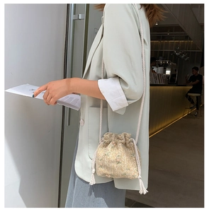 Détail de broderie florale sur petit sac seau en paille beige avec cordon en coton