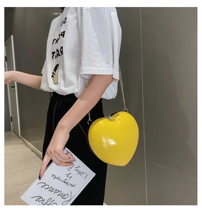 Detailed view of glossy yellow heart shaped crossbody bag with gold chain on model