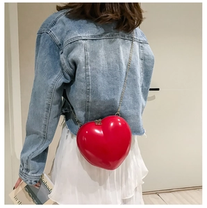 Detail view of heart-shaped red patent leather shoulder bag with golden chain strap on a model