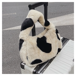 Détail du sac hobo en peluche à motif vache accroché à une valise pour l'automne hiver