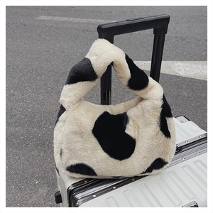 Vue détaillée d'un sac seau en peluche à motif vache accroché à une valise argentée