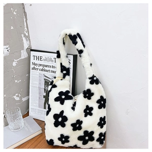 Close-up of soft white plush handbag featuring black flower patterns on a wooden surface