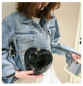 Detail showing a heart-shaped black patent leather bag with a sleek metal chain strap